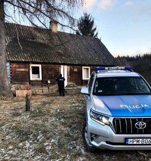 Radiowóz pod drewnianym domem, w tle policjant