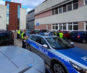 Policjanci stojący obok radiowozów na terenie szpitala.